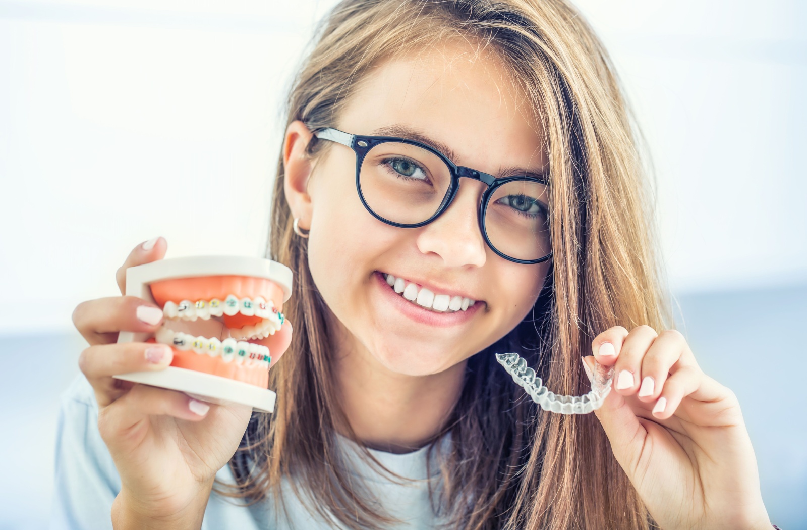 Girl comparing braces and Invisalign aligner at the dentist.