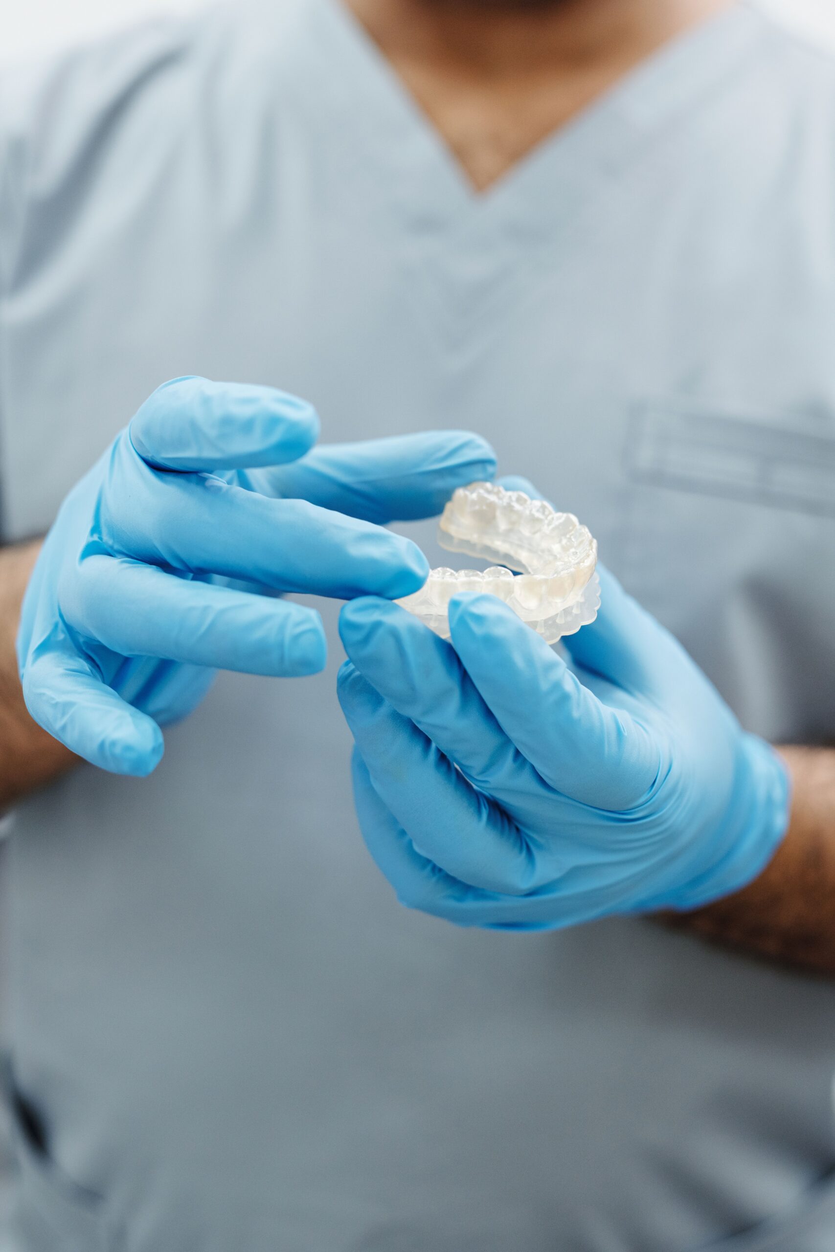 A close-up of a smiling patient holding a clear aligner